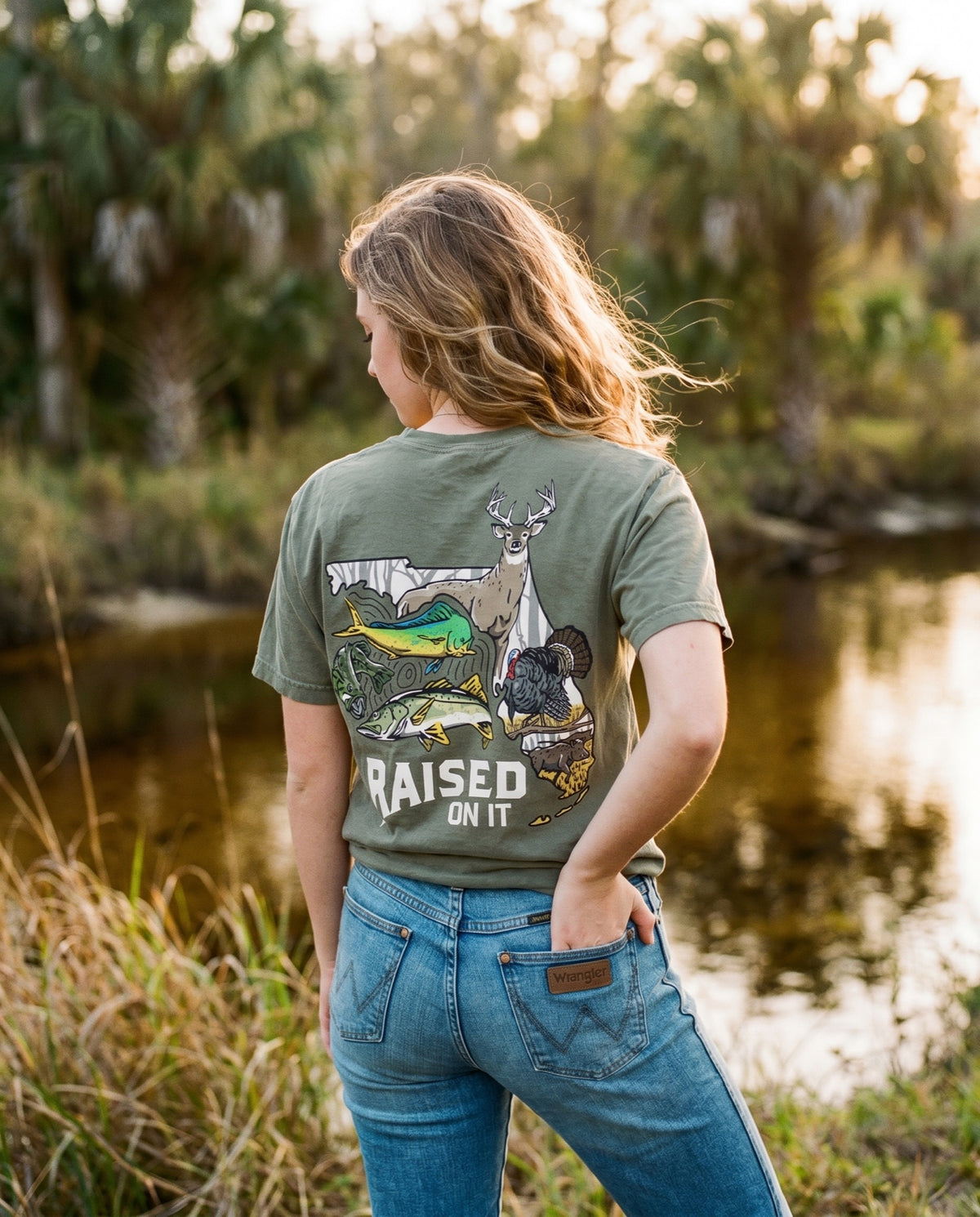 Woman wearing the olive Florida Sportsman Tee by a Florida creek, full back print visible